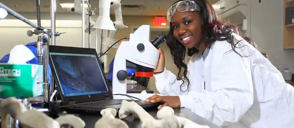female student wearing lab coat in front of microscope