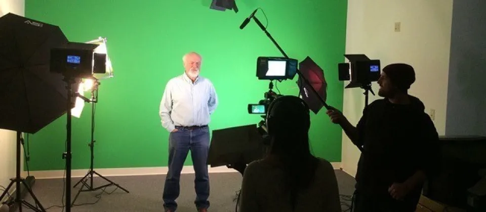 male standing in green room with lights and cameras