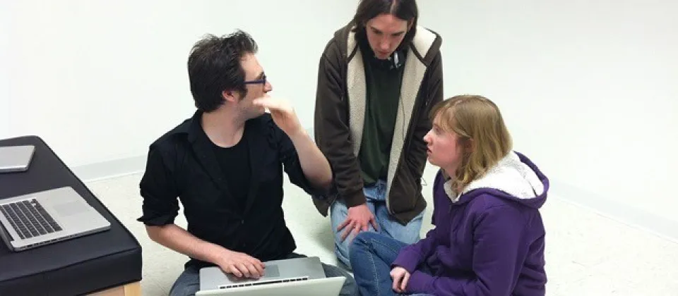 male professor sitting on floor with computer and students