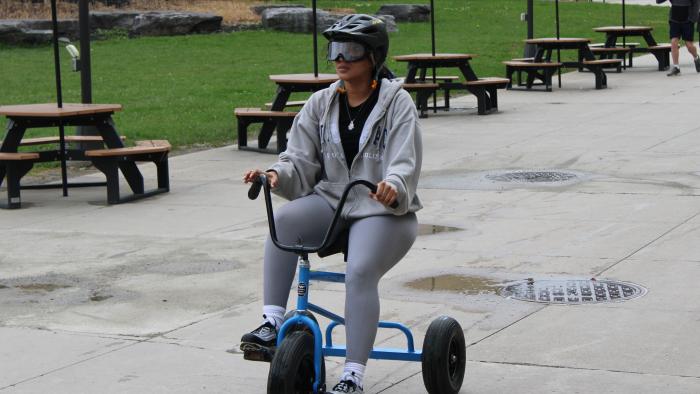 Students rides a tricycle with drunk goggles on.