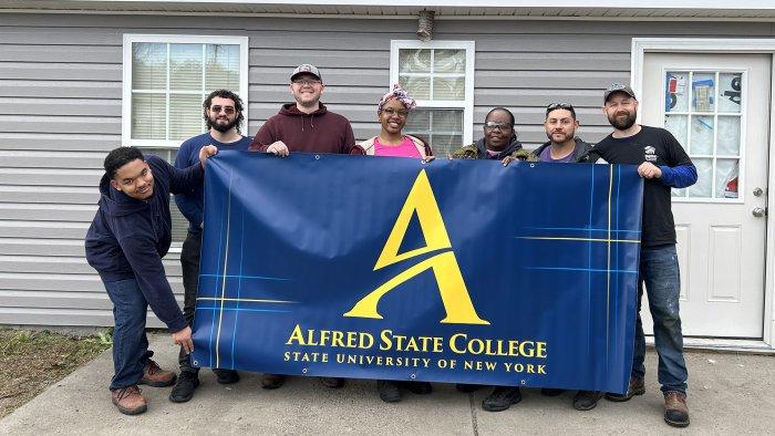 Students hold up Alfred State banner at Habitat for Humanity site.