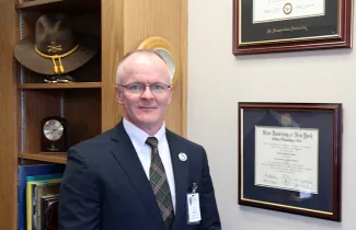 Jim Helms stands near his Alfred State diploma in his office