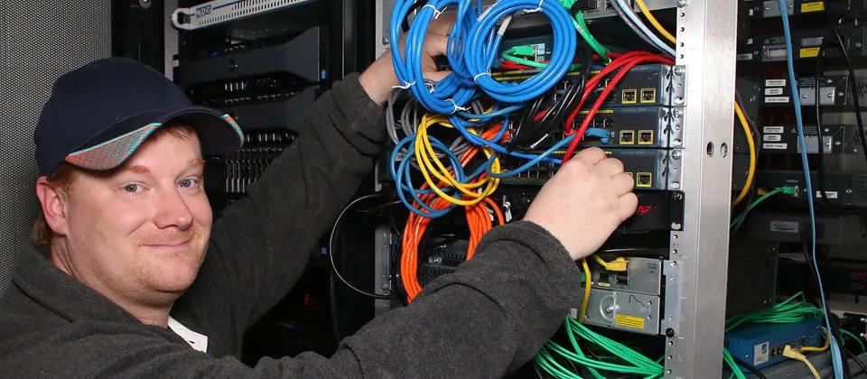Student connecting ethernet cables to network switch on rack.
