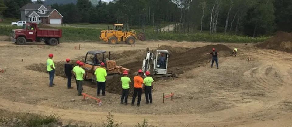 People outside with heavy machinery digging hole in ground.