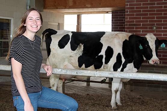Madeline Keyes stands in front of a cow at the farm