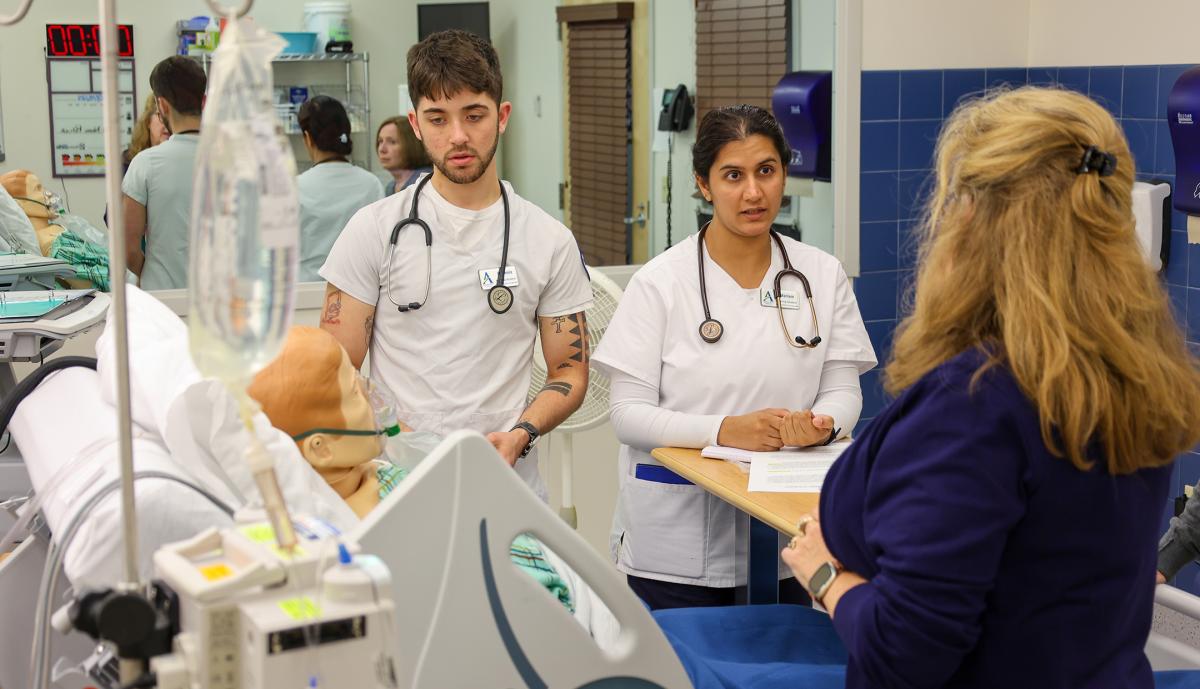 students work with a professor in a nursing lab