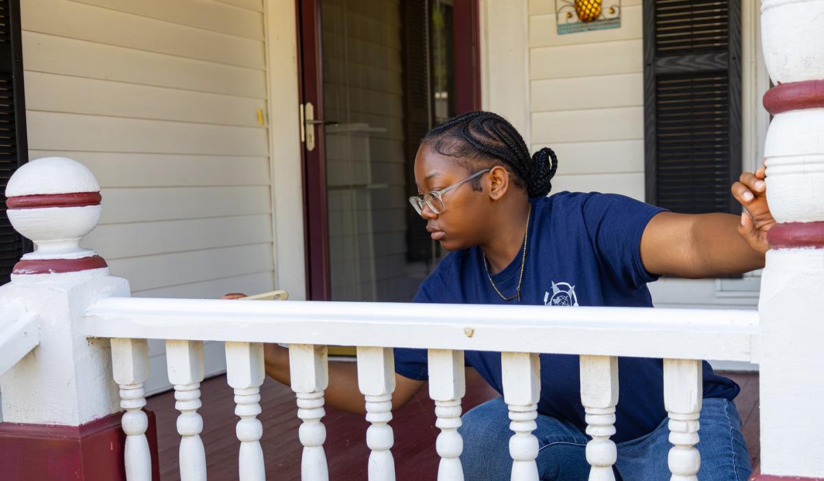 student paints a railing for a resident