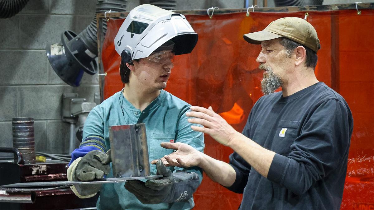Professor speaks with a student in a welding lab