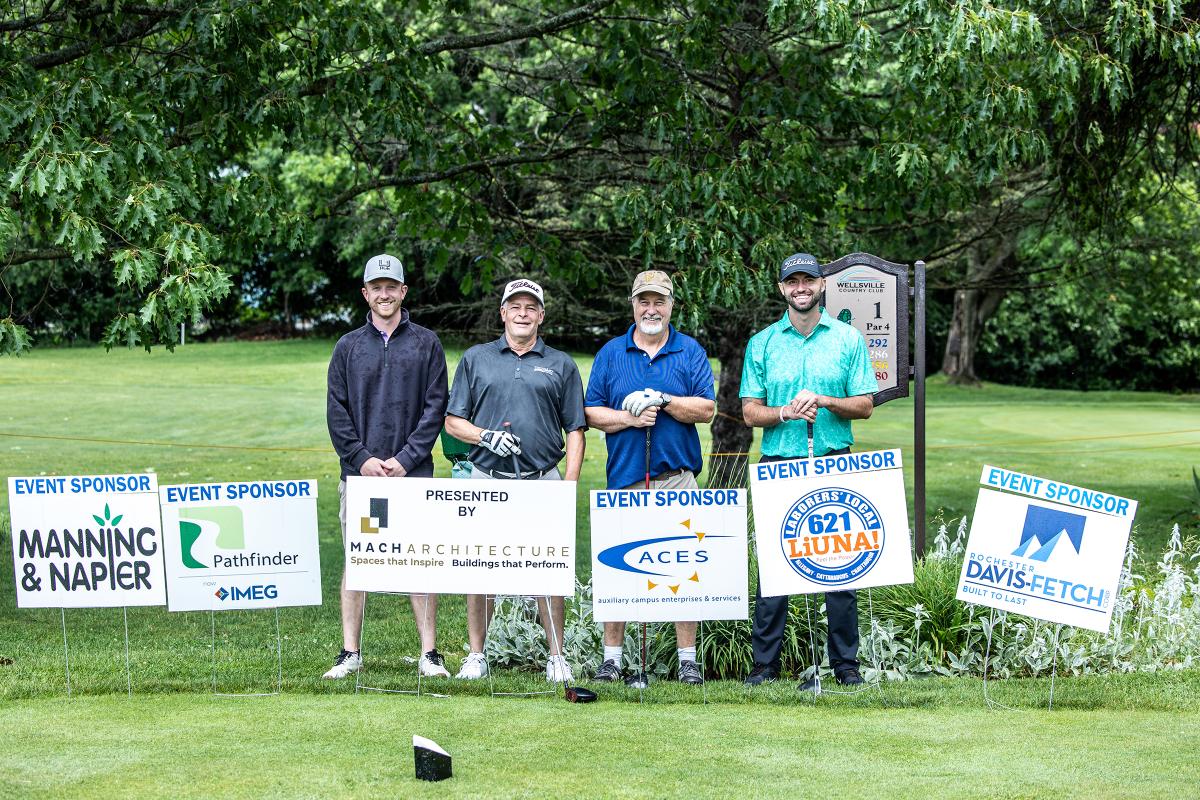 Winning team of the Alfred State golf tournament standing behind tournament sponsor signs
