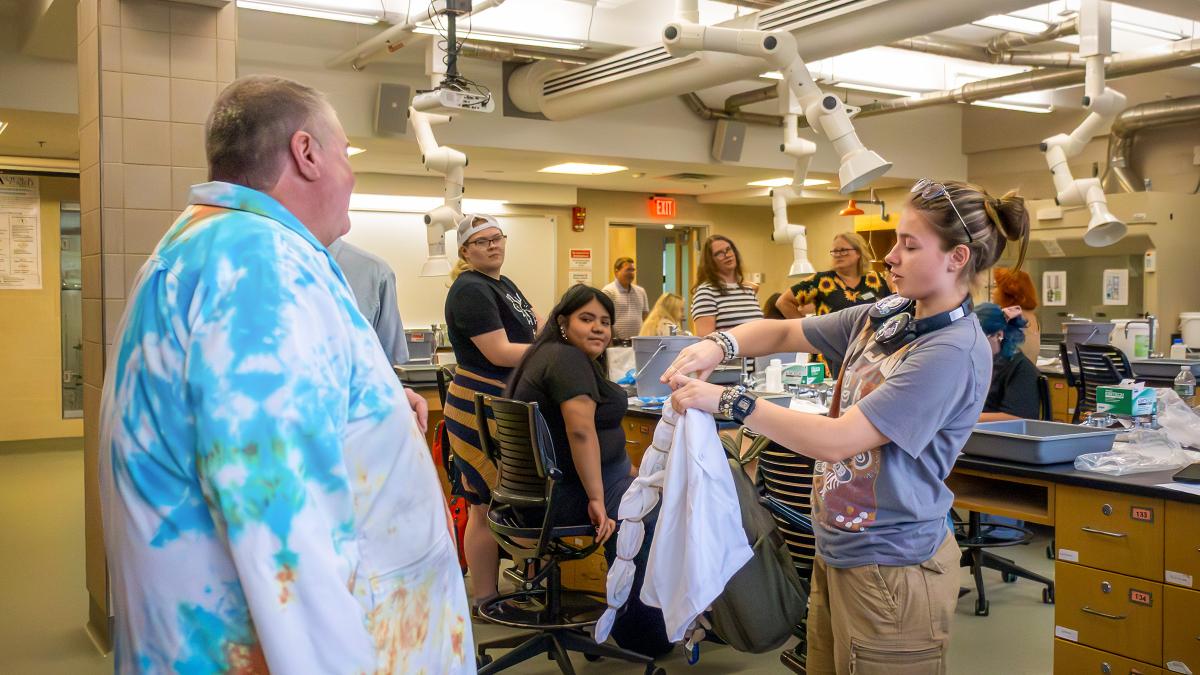 Students and an instructor participate in a hands on textile dyeing activity in a laboratory classroom, demonstrating techniques and discussing project results.
