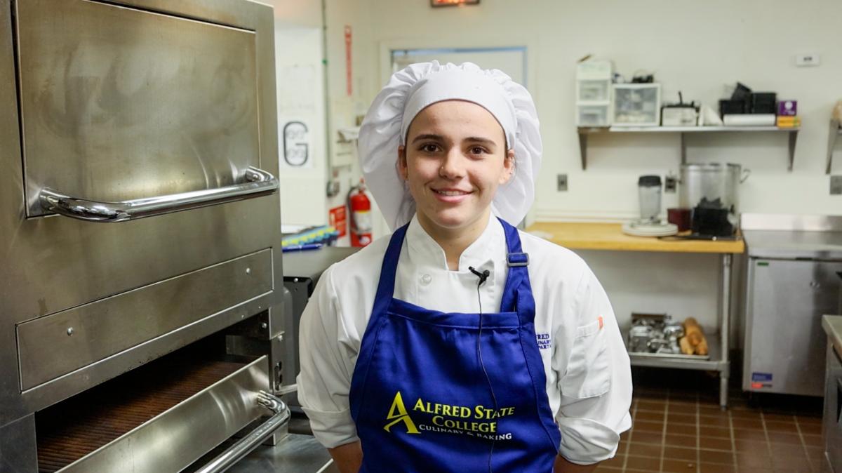 Student poses in a kitchen in front of an oven