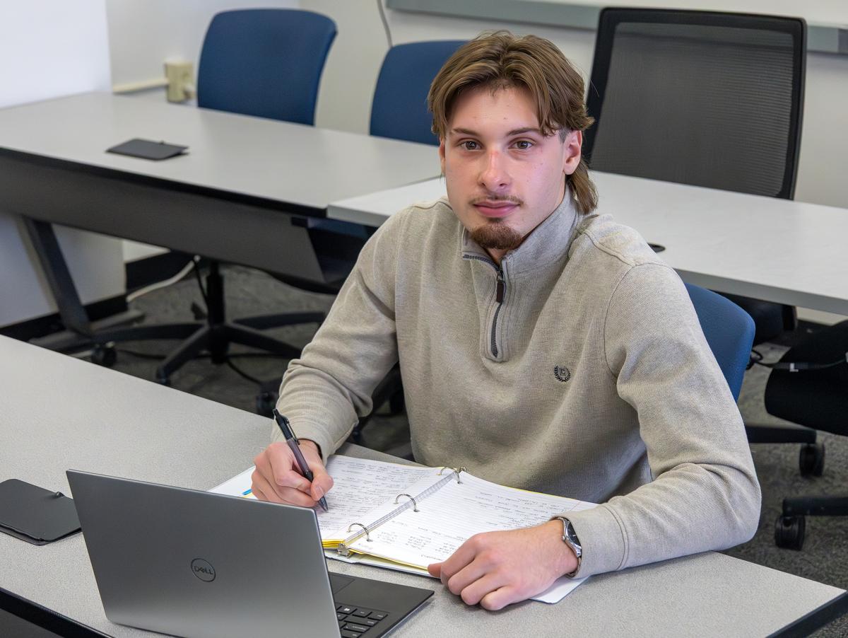 Student takes notes while sitting behind his laptop