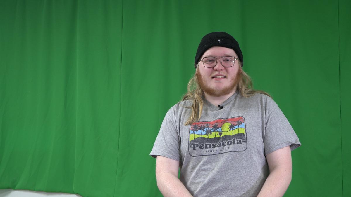student sits in front of a green screen