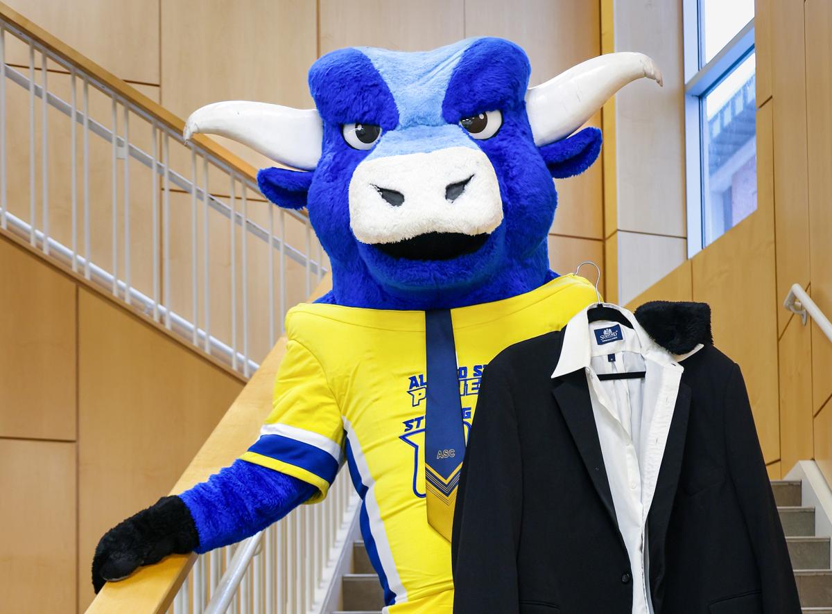 Big Blue stands on the stairs holding a suit