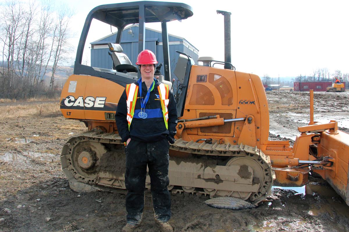 Conor Compton poses by a bulldozer with his medals from the Allegany-Empire Championships. Compton will compete at the NCAA Championships this week.