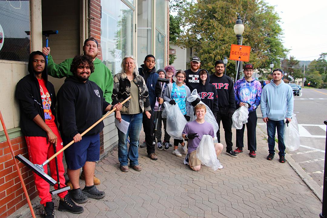Students take a break to pose outside downtown businesses during the Day of Service. Students from Alfred State and Alfred University joined the community to spruce up areas around Main St.