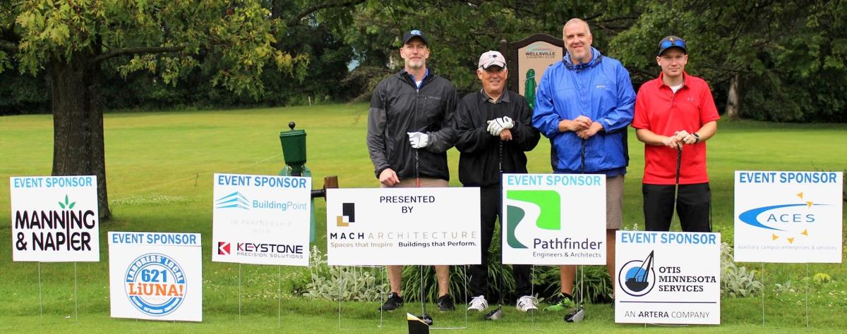A foursome stands in front of tournament sponsor signs at the Alfred State Golf Tournament