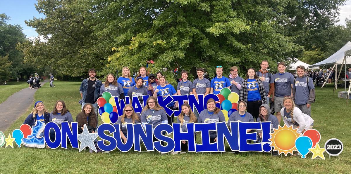 Student stand behind Walking on Sunshine sign