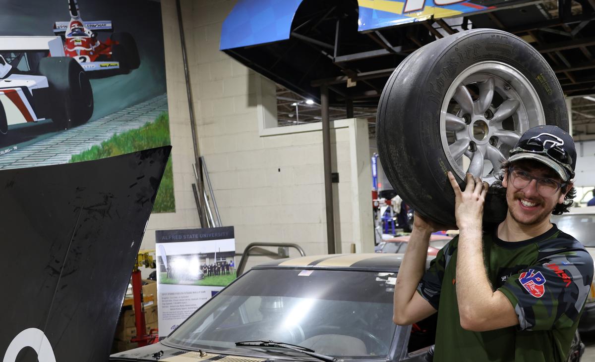 Quinn Scanlon holds a tire in front of a car.