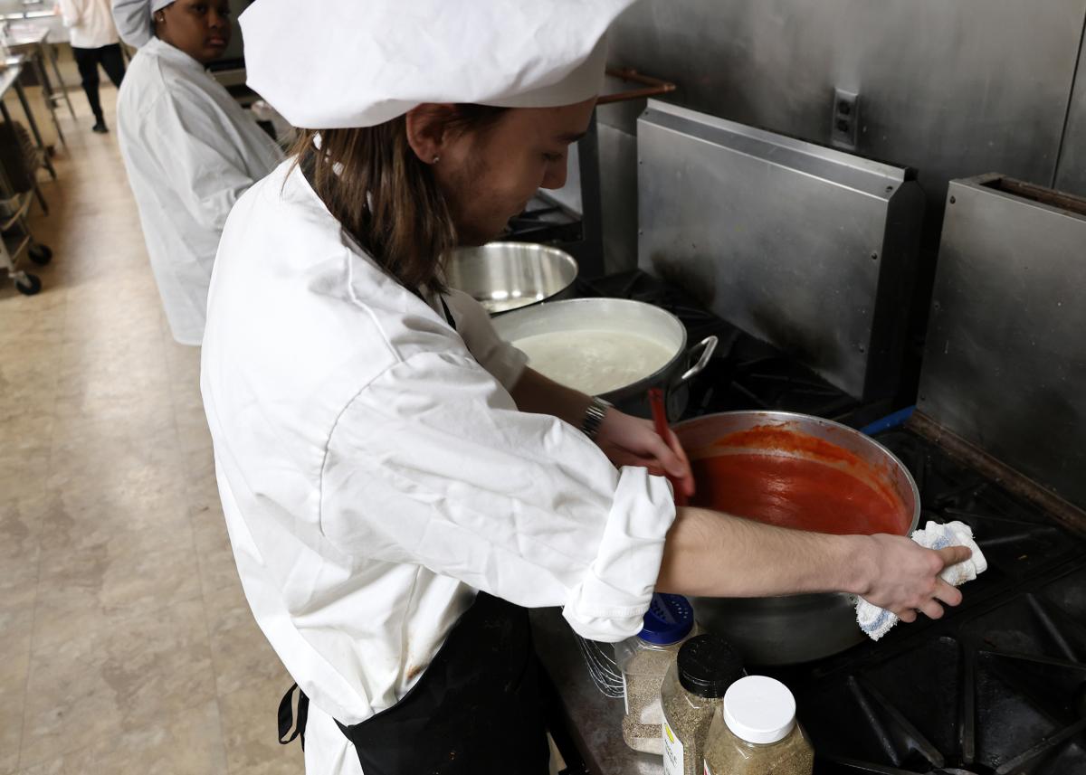 student stirs spaghetti sauce