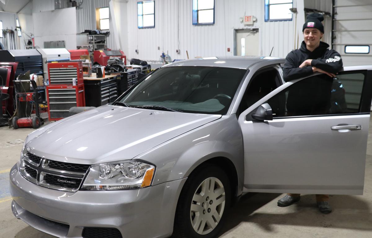A student stands with the 2014 Dodge Avenger