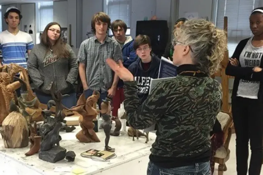 Students listening to professor in classroom with sculptures on table.