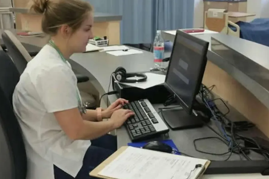 Healthcare management student working on computer at desk in hospital environment.