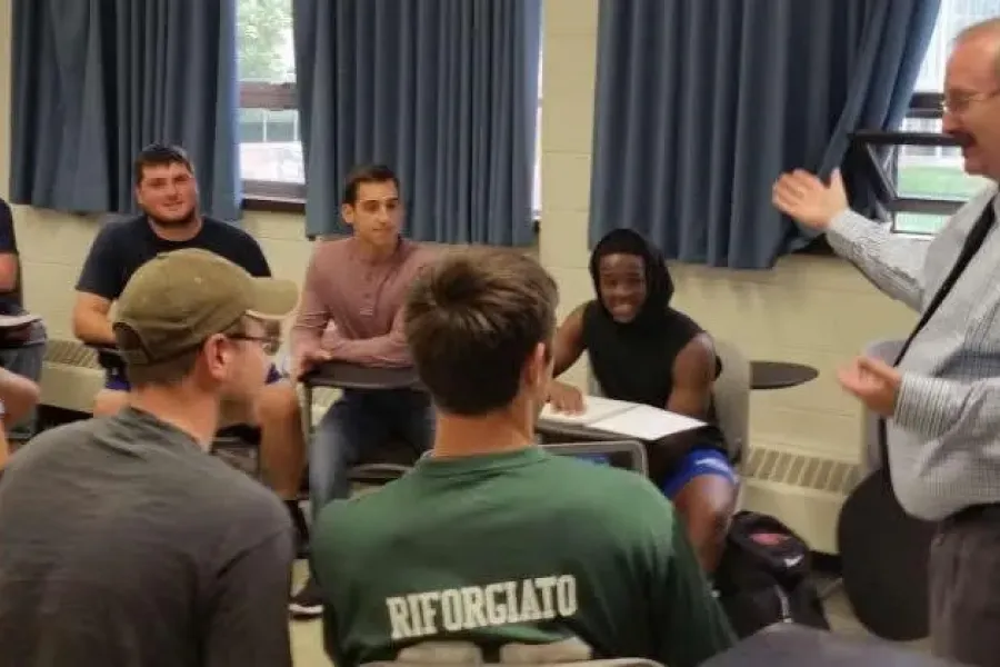 Students sitting at desks in classroom listen to professor.