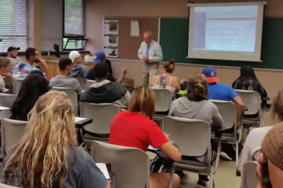 Students sitting as desks in a classroom with the professor in front.