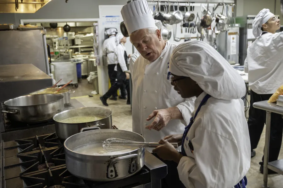 A student in a kitchen chopping vegetables
