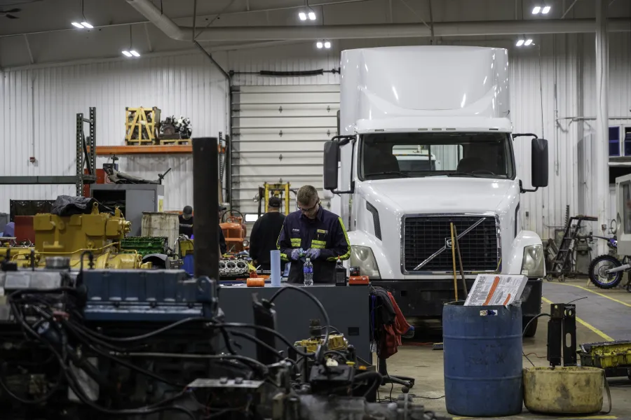 A student in an automotive bay standing in front of a large truck