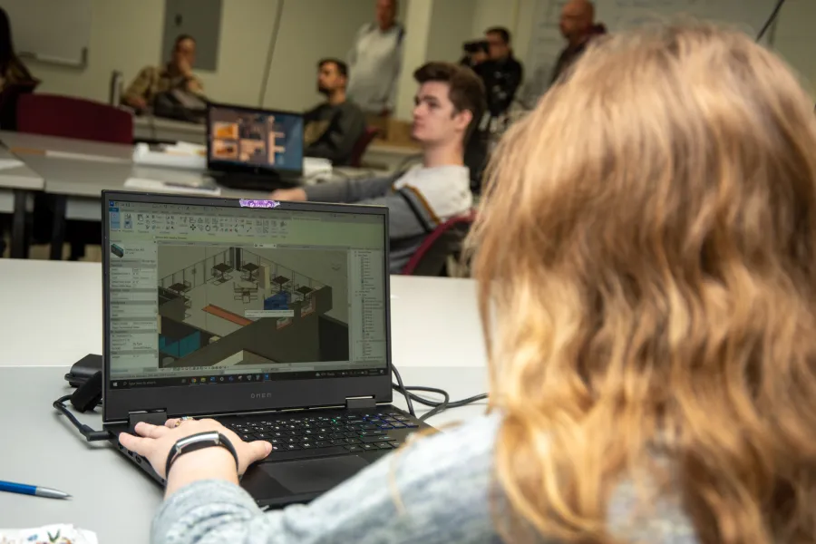 Student working on laptop with CAD software visible.