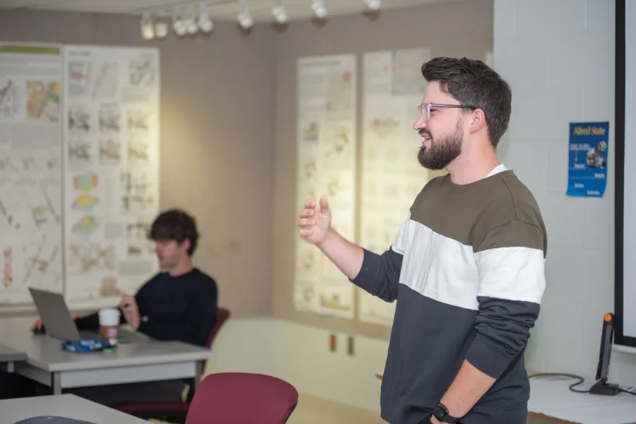A male professor standing in front of architectural drawings while teaching a group of students