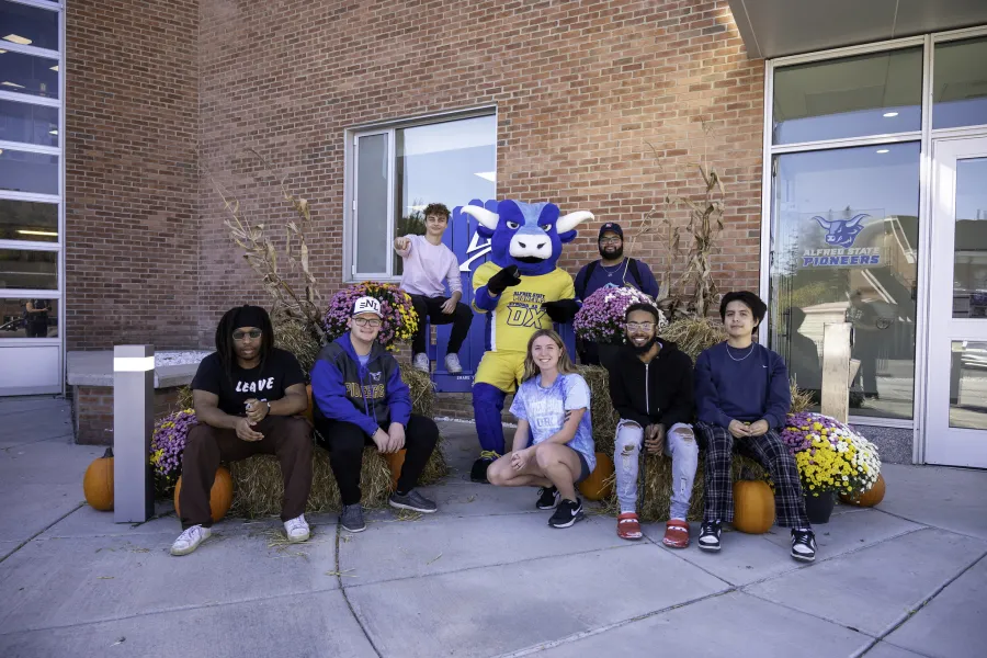 Students sitting and on hay bales with Alfred State's mascot.