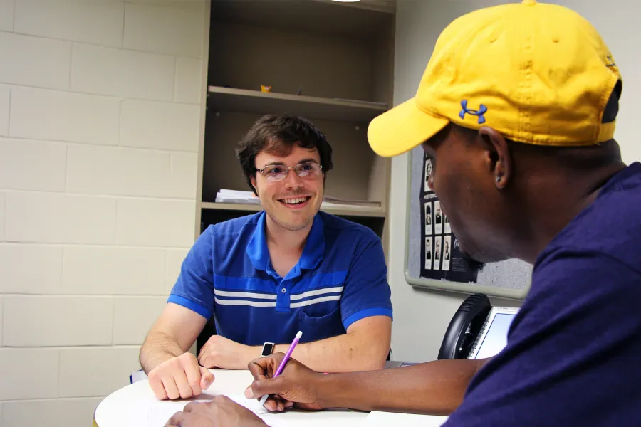 A staff member helping mentor a student wearing a yellow hat.