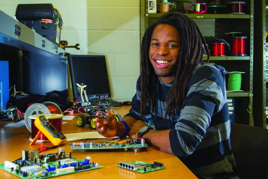 A student sitting with a small robot and computer equipment