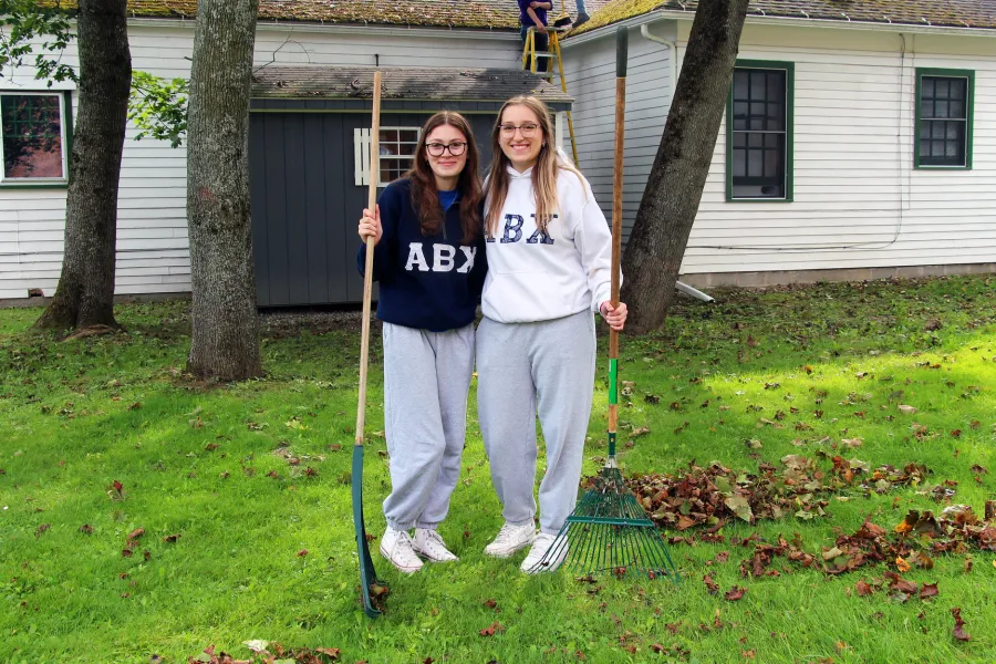 Two girls holding rakes next to a pile of leaves