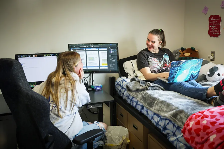 Two students talking while working on computers in a residence hall room