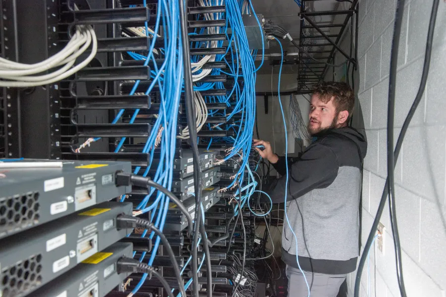 A student in a room full of computers and blue wires.