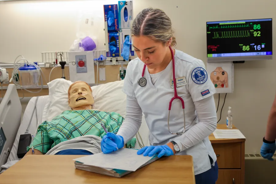 Nursing student taking notes in practice hospital environment.