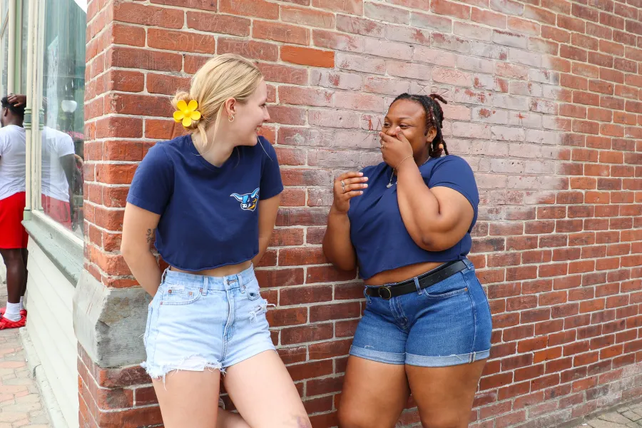 two students standing an laughing against a brick wall