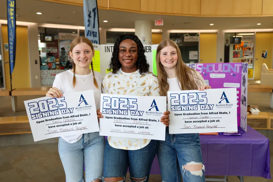 Three female students holding signs that showcase where they have accepted job offers from upon graduation.