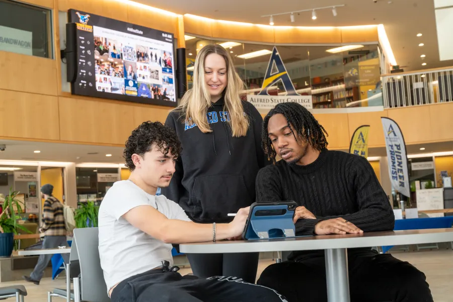 Three students sitting at a table working together on a digital tablet.