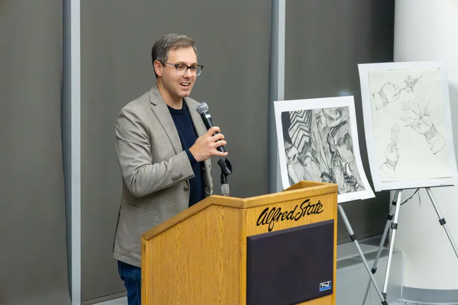 A professor at a podium presenting next to two art pieces.