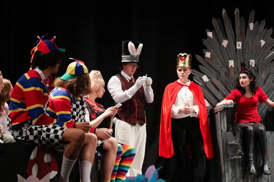 Students dressed as the characters from Alice in Wonderland while acting on a stage.