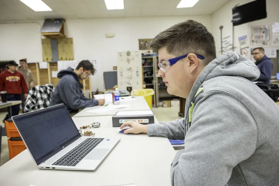 A student wearing safety glasses working on a laptop.