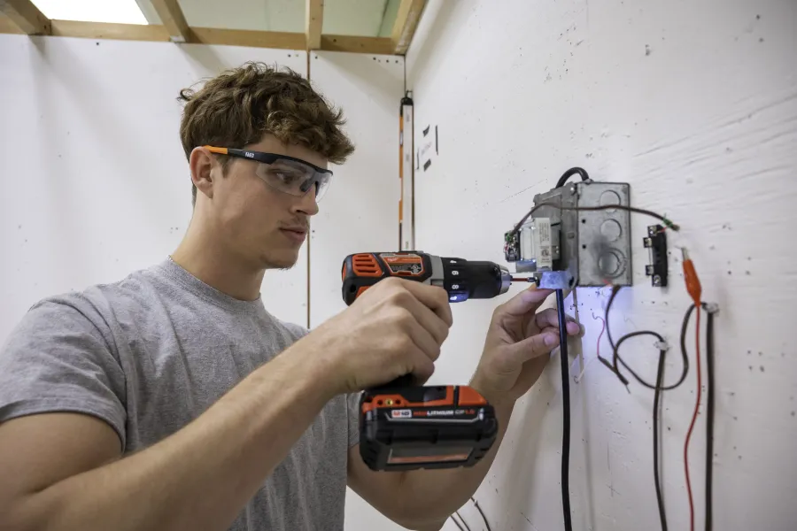 A student with a drill installing an outlet.