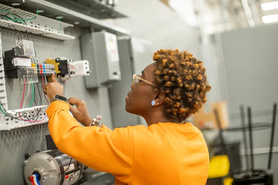 A student wearing a orange/yellow shirt looking at electrical wiring.