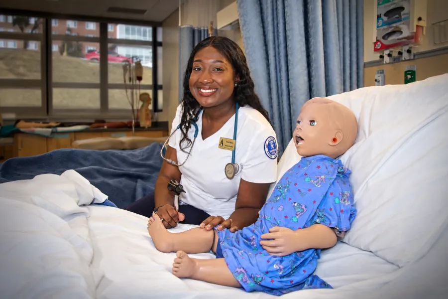 A nursing student sitting next to a manekin.
