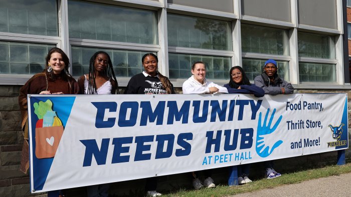 The Civic Leadership student ambassadors stand behind the Community Needs Hub sign. The Community Needs Hub is now open on the ground floor of Peet Hall.